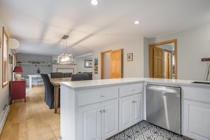 A modern kitchen with a built-in dishwasher, a dining area with a table and chairs, and a hallway leading to another room.