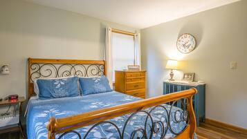 A bedroom with a wooden bed, a dresser, a bedside table with a lamp, and a wall clock.