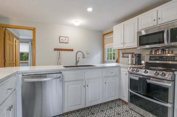 A kitchen with white cabinets, a stainless steel dishwasher, a double oven, and a microwave.