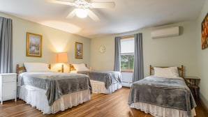 A hotel room with two beds, a ceiling fan, a window with curtains, a bedside table, and a wall-mounted air conditioner.