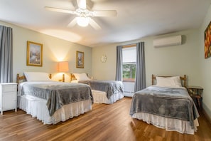 A hotel room with two beds, a ceiling fan, a window with curtains, a bedside table, and a wall-mounted air conditioner.