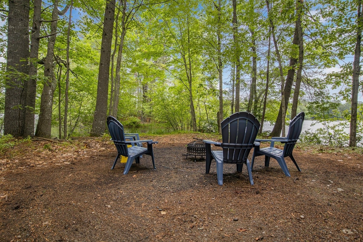 A campsite with two Adirondack chairs facing a lake, surrounded by trees.