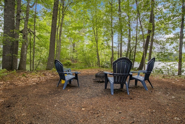 A campsite with two Adirondack chairs facing a lake, surrounded by trees.