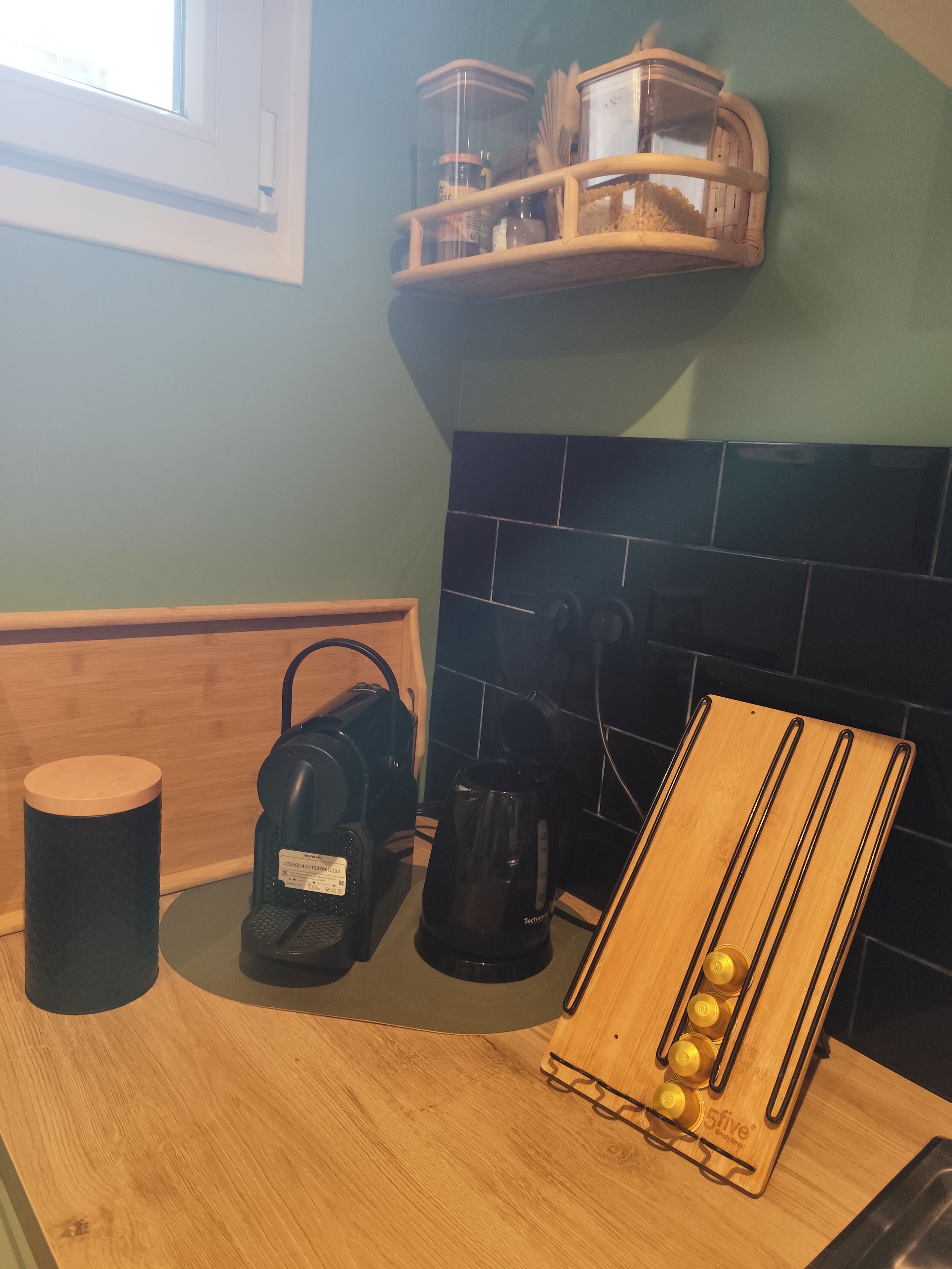 Una cocina con encimera de madera, cafetera, hervidor y una estantería de madera con botellas.