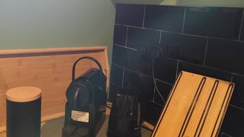Una cocina con encimera de madera, cafetera, hervidor y una estantería de madera con botellas.