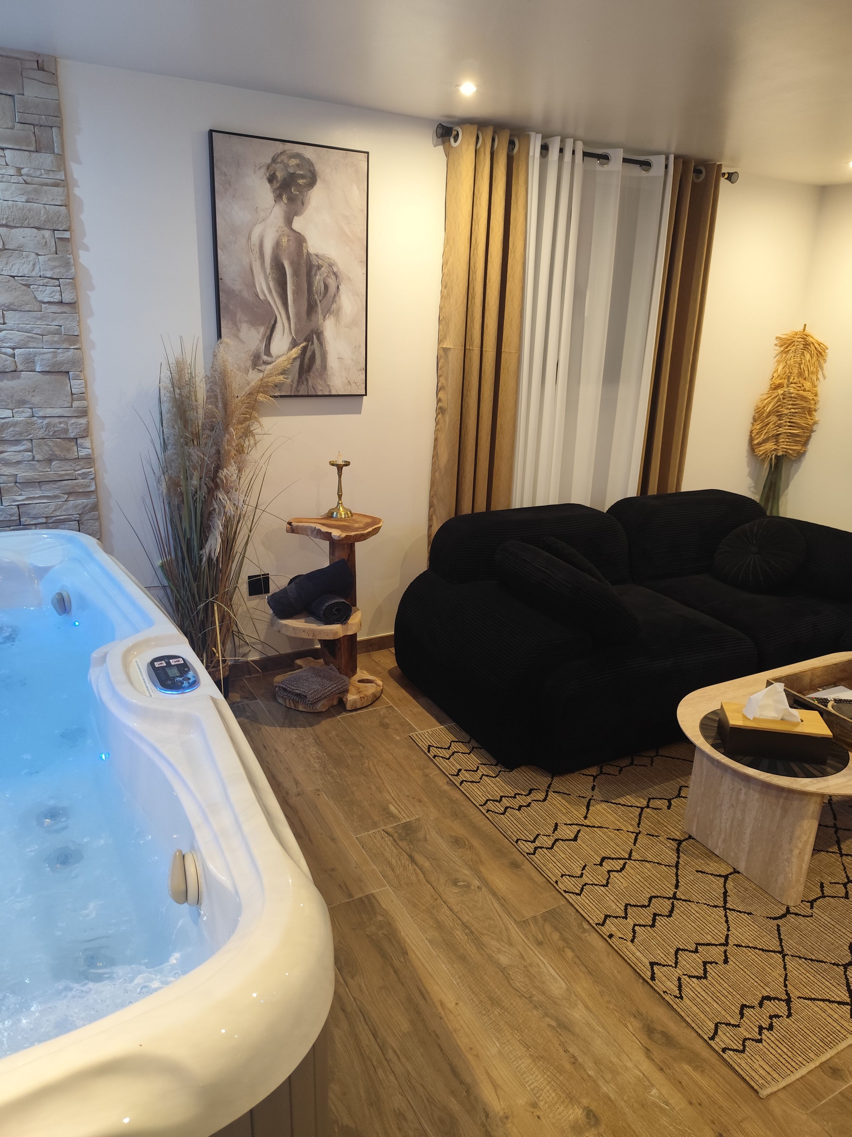 Uma sala de estar moderna com uma banheira de hidromassagem, um sofá preto, uma mesa de centro de madeira e um quadro na parede.