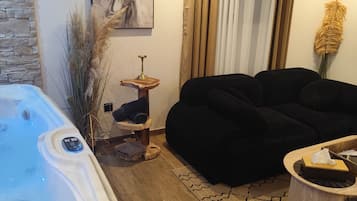 Uma sala de estar moderna com uma banheira de hidromassagem, um sofá preto, uma mesa de centro de madeira e um quadro na parede.