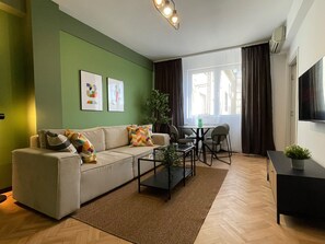A modern living room with a sofa, coffee table, and a dining area with chairs. There are two framed artworks on the wall, a potted plant, and a flat-screen TV mounted on the wall. - Chill Flow Calea Victoriei next to The Old Town (București)