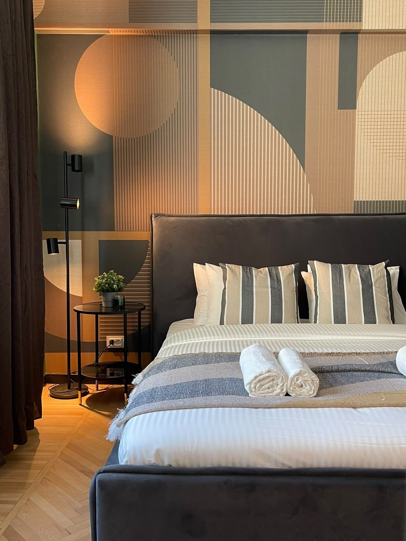 A modern hotel room with a large bed, a bedside table with a lamp, and a view of the cityscape.