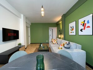 A modern living room with a flat-screen TV, a dining table, and a sofa with colorful cushions. - Chill Flow Calea Victoriei next to The Old Town (București)