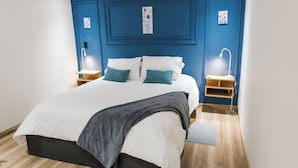 A bedroom with a bed, bedside tables, lamps, and a blue accent wall. - Hotel 664 (Poblado)