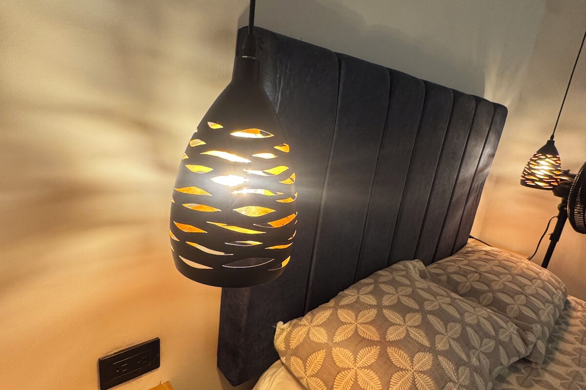 A bedroom with a bed, a bedside table, and a hanging lamp.