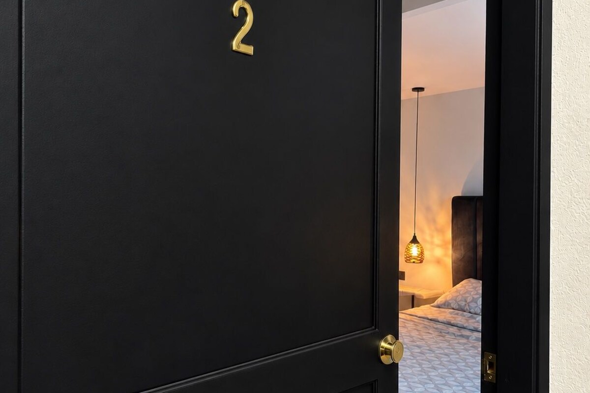 A black door with the number 2, leading to a bedroom with a bed and a hanging light fixture.