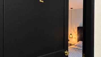 A black door with the number 2, leading to a bedroom with a bed and a hanging light fixture.