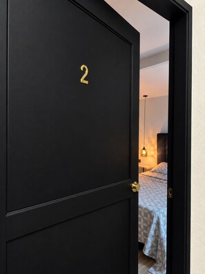 A black door with the number 2, leading to a bedroom with a bed and a hanging light fixture. - Hotel 664 (Medellin)