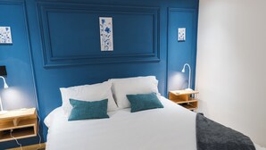 A bedroom with a bed, two pillows, a bedside table, a nightstand, a lamp, and a wall-mounted shelf. - Hotel 664 (Poblado)
