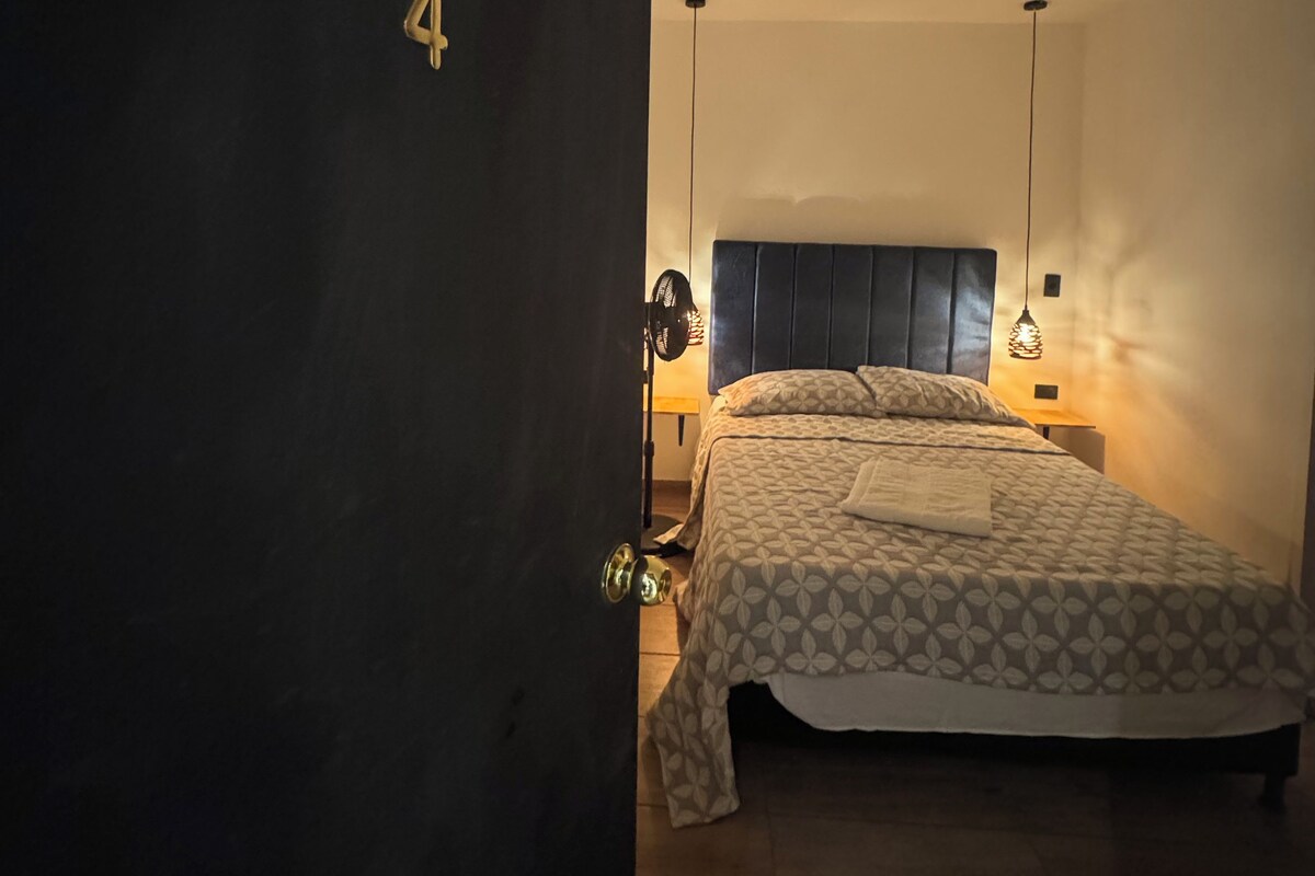 A bedroom with a bed, a nightstand, a lamp, and a door with a number.