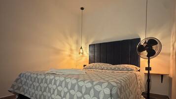 A bedroom with a bed, a bedside table, a wall-mounted fan, and a hanging light fixture.