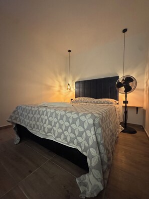 A bedroom with a bed, a bedside table, a wall-mounted fan, and a hanging light fixture. - Hotel 664 (Medellin)