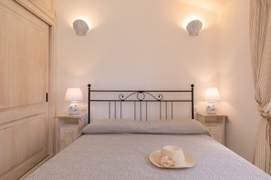 A bedroom with a bed, two bedside lamps, a decorative wall light, and a curtain. - Villetta Rosella by Wonderful Italy (Golfo Aranci)