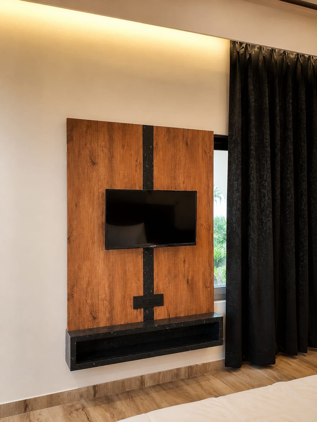 A modern living room with a flat-screen TV mounted on a wooden panel wall, a black shelf below, and a window with black curtains.