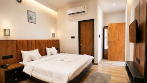 Een moderne slaapkamer met een houten hoofdbord, een bed met wit beddengoed, een nachtkastje met een lamp, een aan de muur bevestigde televisie en een houten garderobe.