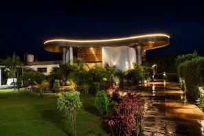 A modern building with a unique curved roof structure, surrounded by well-maintained gardens and a paved pathway. - Royal Reef Resort (Depalpur)
