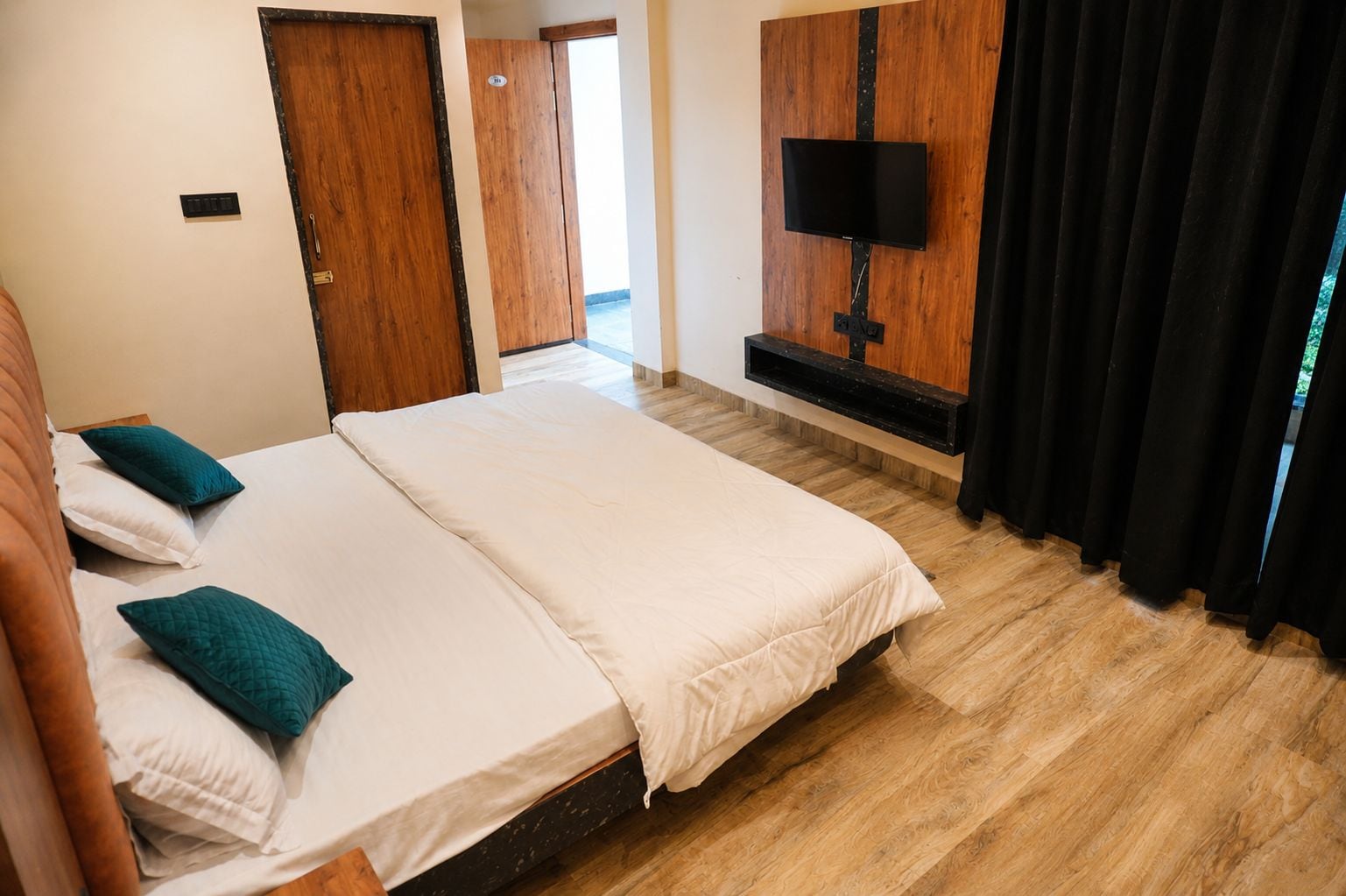 Hotellihuone, jossa on parivuode, seinälle asennettu taulutelevisio ja puulattia.