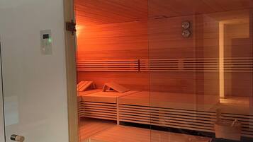 A sauna with wooden benches and a glass partition, a control panel, and a clock on the wall.