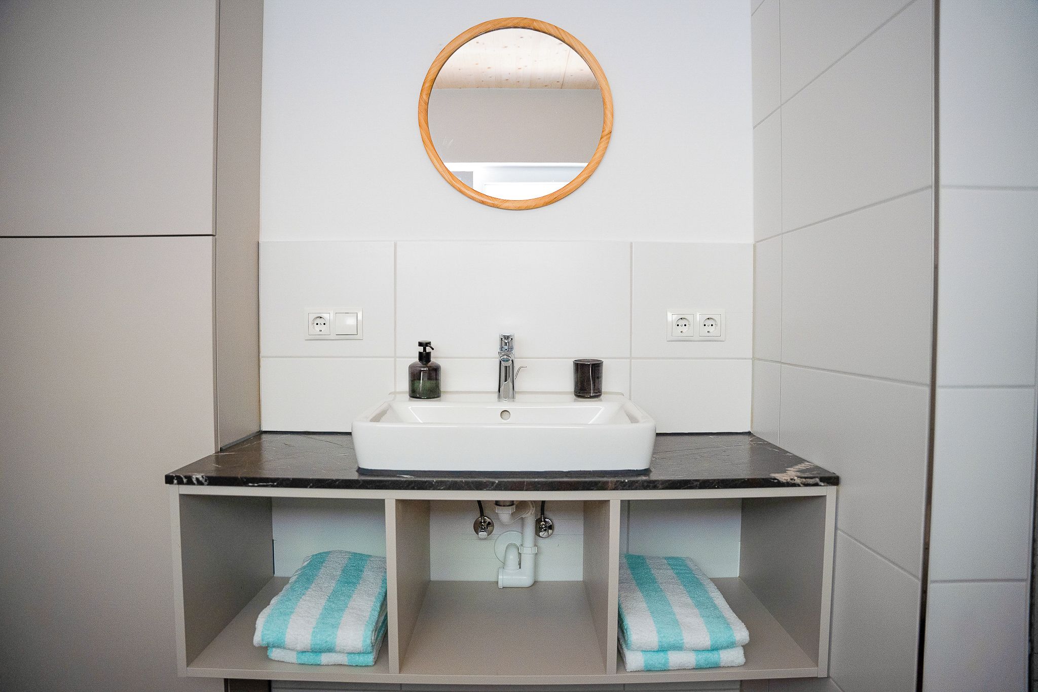 A bathroom with a white sink, a mirror, and two towel racks with towels.