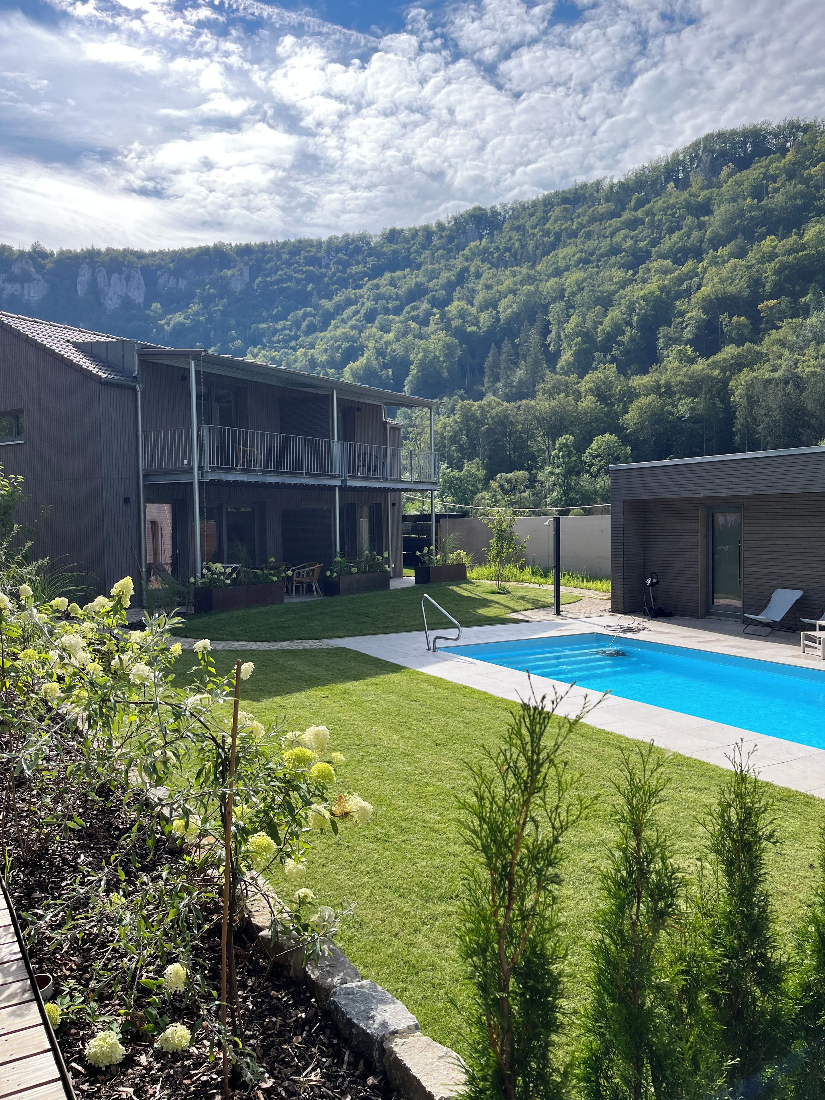 A residential area with a swimming pool, a two-story building with a balcony, and a mountainous backdrop.