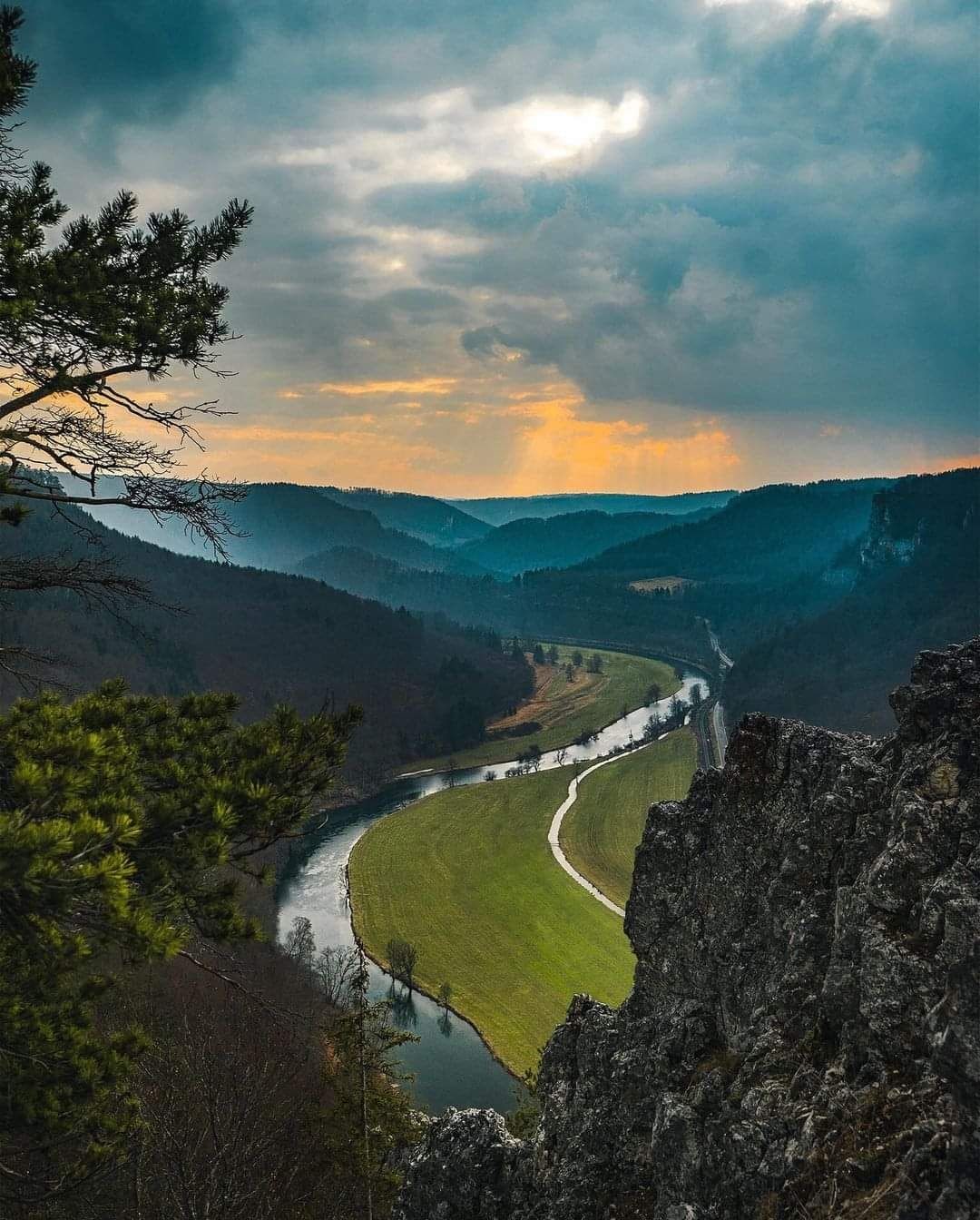 Un río serpentea por un valle, con una carretera que lo acompaña, rodeado de colinas boscosas.