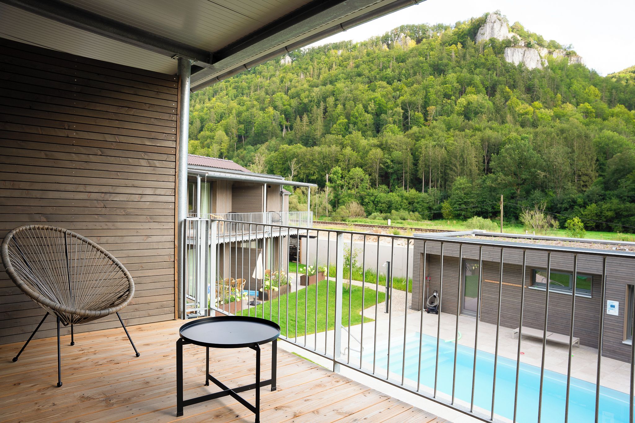 Un balcón con vistas a un paisaje boscoso, una piscina y una silla.