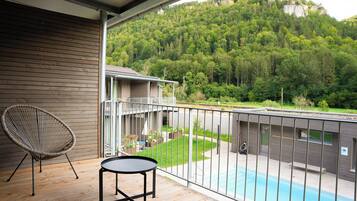 Un balcón con vistas a un paisaje boscoso, una piscina y una silla.