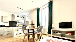 A modern living room with a dining area, a kitchen, and a TV. - Charmant T2 avec Terrasse et Jardin - Le Gamay (Châtel-Guyon)