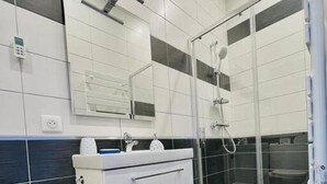 A modern bathroom with a glass shower enclosure, a white vanity with a mirror, and black and white tiled walls. - Charmant T2 avec Terrasse et Jardin - Le Gamay (Châtel-Guyon)