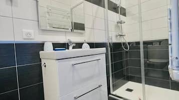 A modern bathroom with a glass shower enclosure, a white vanity with a mirror, and black and white tiled walls.