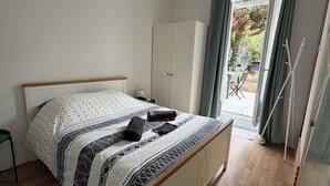 A bedroom with a bed, a wardrobe, and a view of the outdoors. - Charmant T2 avec Terrasse et Jardin - Le Gamay (Châtel-Guyon)