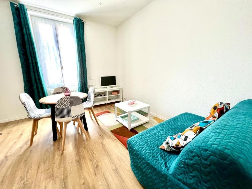 A compact room with a bed, a small table, a chair, a TV, and a window with curtains.