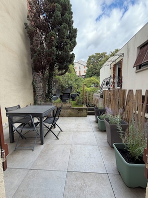 Eine Terrasse mit Tisch und Stühlen, umgeben von Kübelpflanzen und einer Steinmauer.
