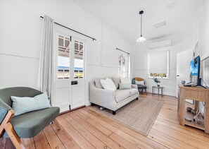 A living room with a sofa, a chair, a TV, and a wooden floor. - Stayawhile Cottage - Heritage 3 Bed in Tenterfield (Tenterfield)