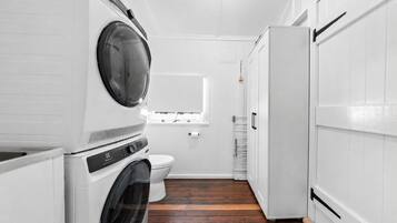 Une petite buanderie aux murs blancs, équipée d’un lave-linge, d’un sèche-linge et de toilettes.