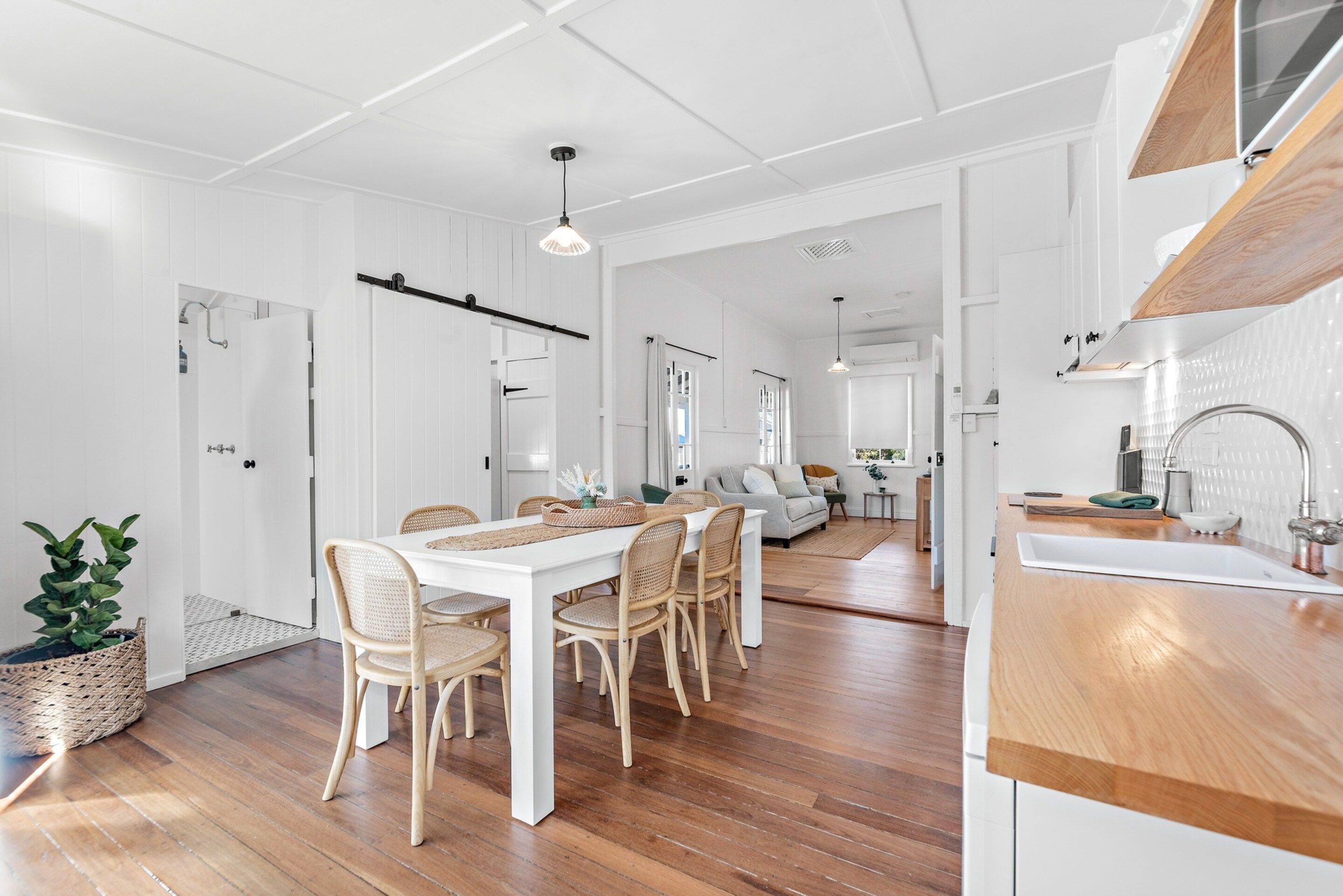 A modern kitchen with white cabinetry, a wooden countertop, and a dining area with a white table and wicker chairs.