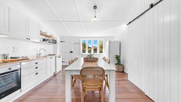 A modern kitchen with white cabinetry, a wooden countertop, and a dining area with a white table and wicker chairs.