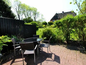 An outdoor patio with a round table and chairs, surrounded by a brick pathway and greenery. - But Dorp 3, Holiday Apartment 3 (Wyk auf Foehr)