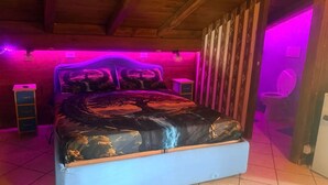 A bedroom with a bed, wooden ceiling beams, a tiled floor, and a purple-lit wall. - Room 'Dea' with Shared Pool, Wi-Fi and Air Conditioning (Santa Marinella)