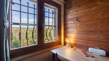Ein Zimmer mit zwei Fenstern, einem Holztisch mit Lampe und Blick auf eine Landschaft.