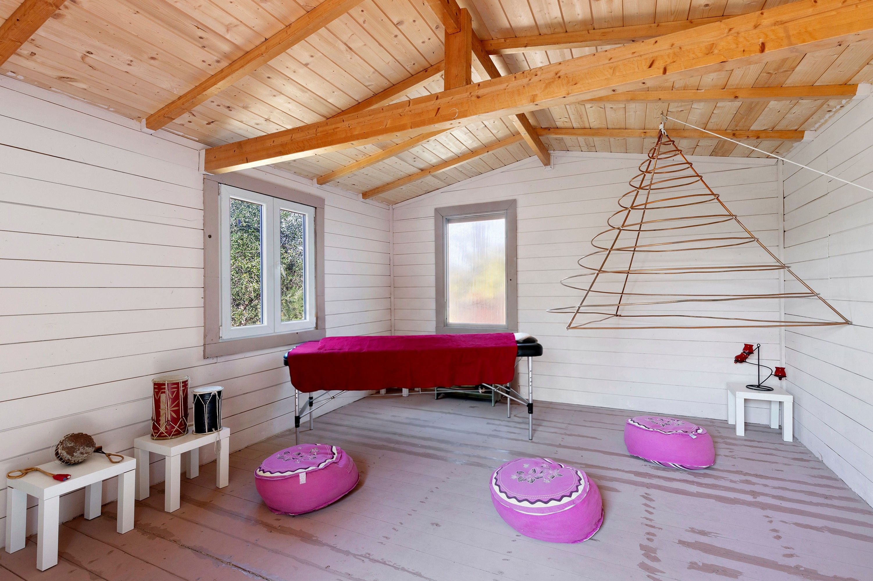 Una habitación con techo de madera, una mesa roja y dos pufs morados.