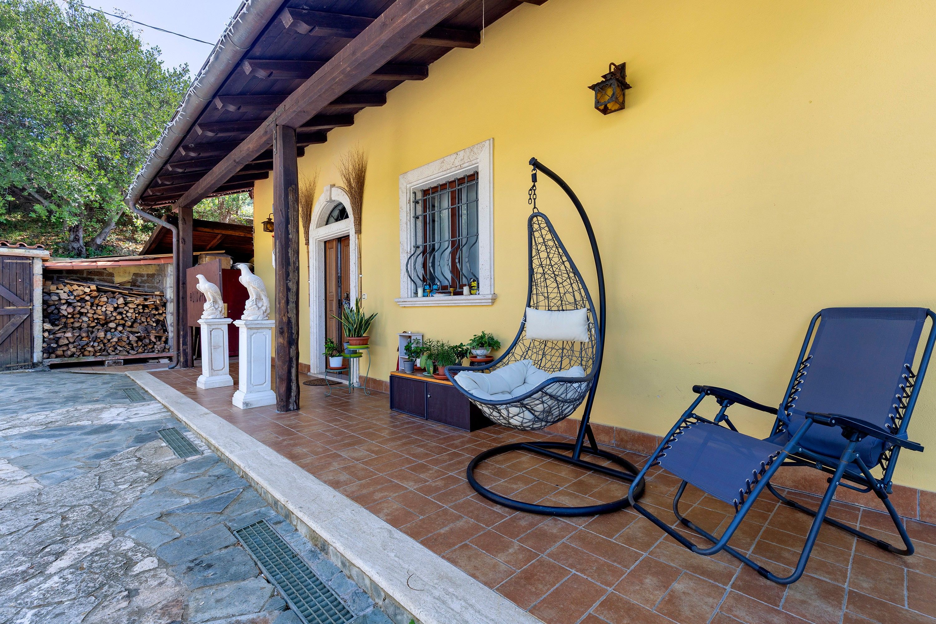 A yellow building with a covered patio area, a hanging chair, and a blue lounge chair.