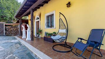 A yellow building with a covered patio area, a hanging chair, and a blue lounge chair.